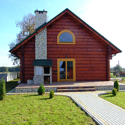 dom z drewna, od boku, kolor drzewna brązowy, okiennice i okna żółte, na ścianie murowany piec.